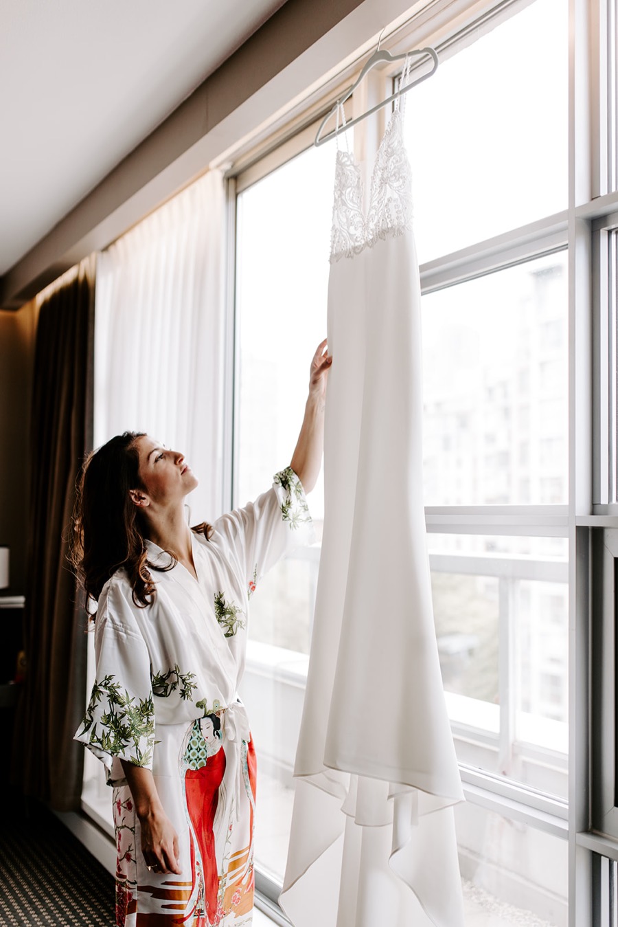 bride looks up at wedding dress hanging in hotel window