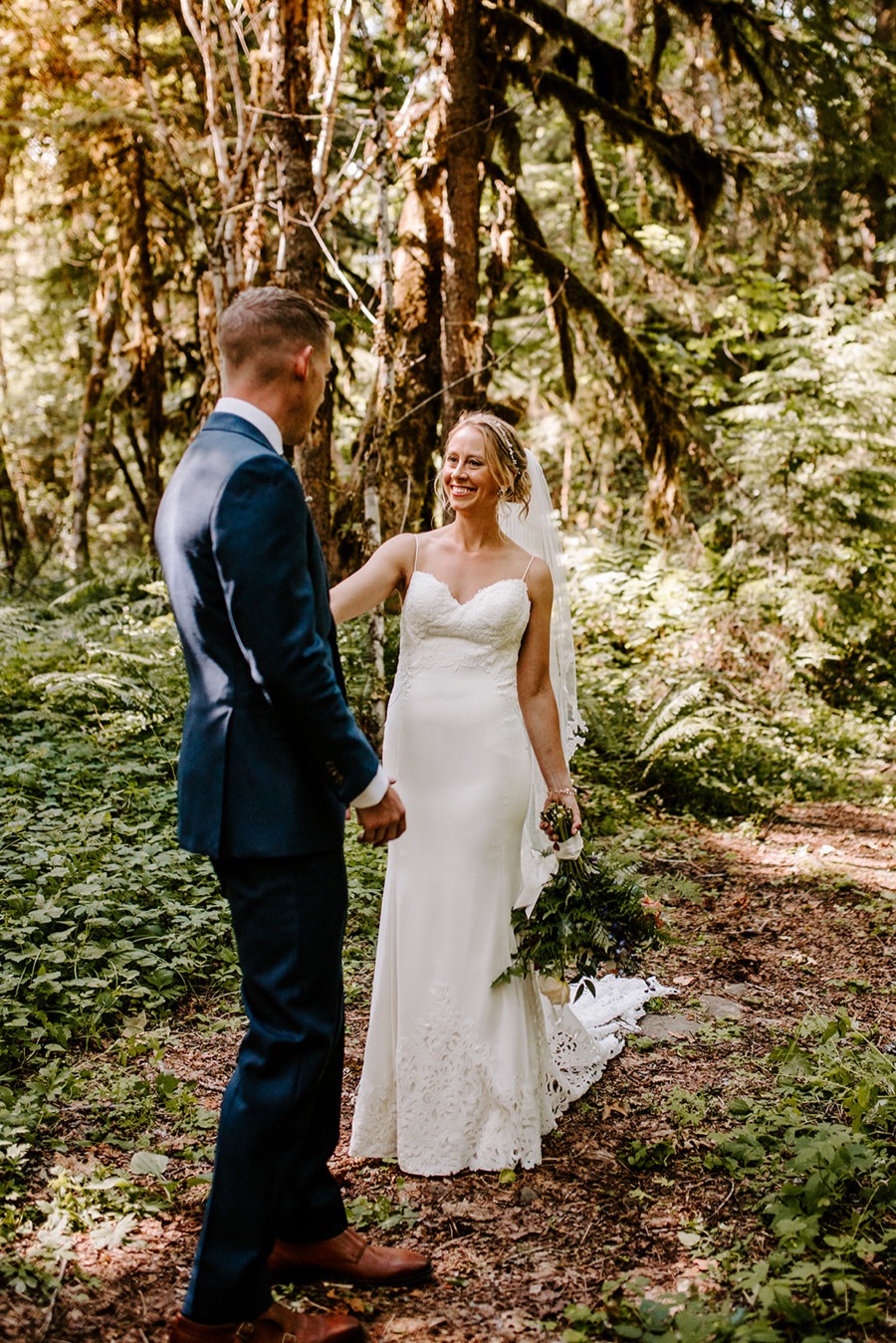 groom turning to look at bride in forest