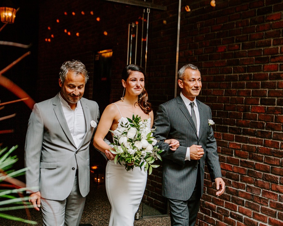 Bride being walked arm in arm by two men