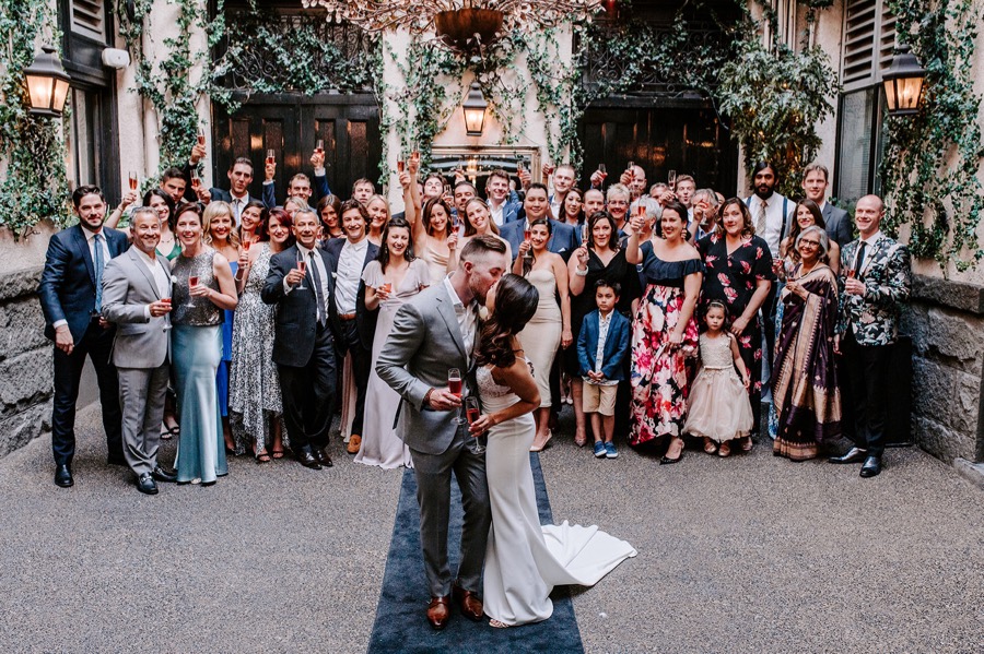 bride and groom kissing passionately as wedding guests cheer behind them