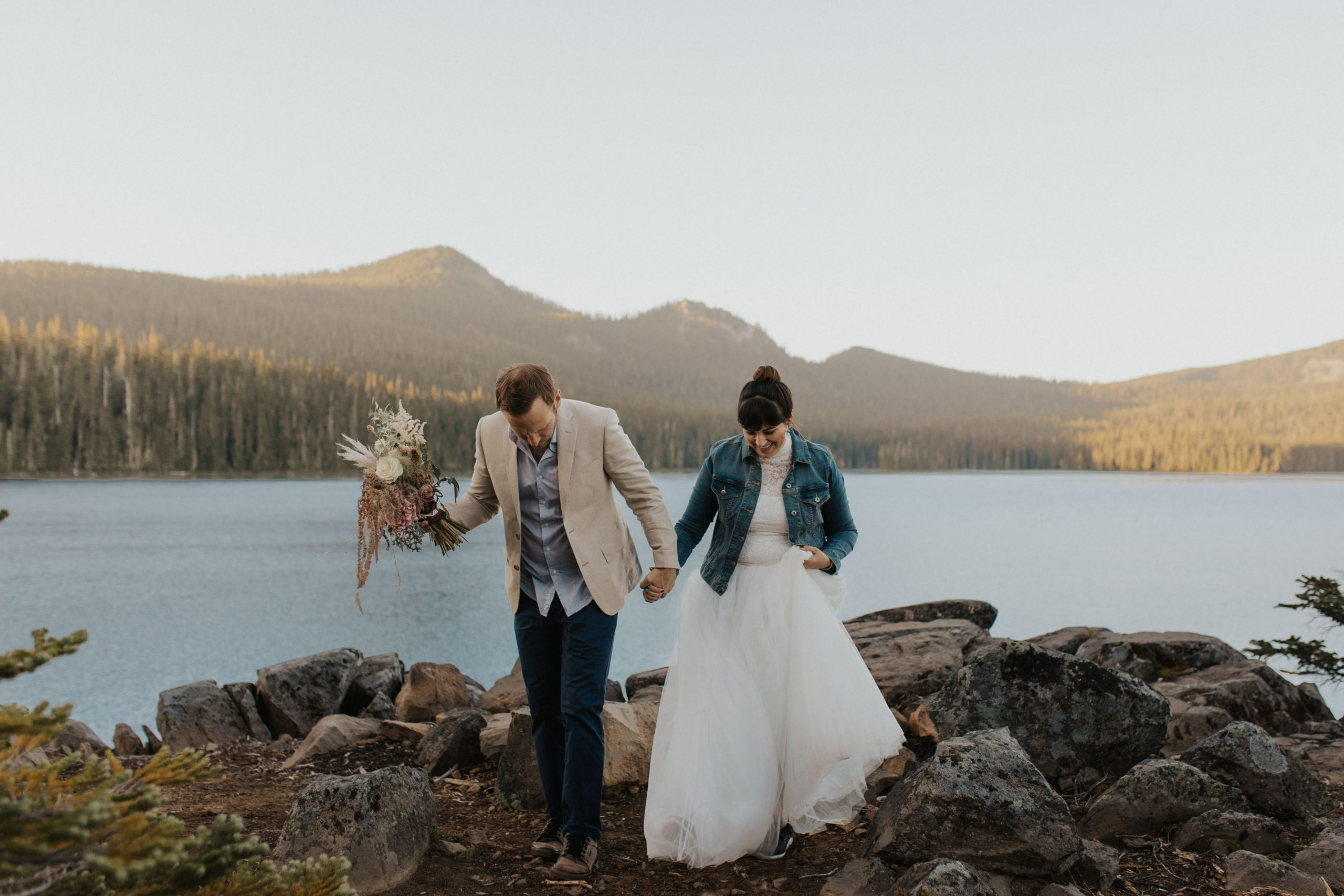 Brennan holds the bouquet while leading Zoraya along the lake shore at Waldo lake for their kayaking elopement
