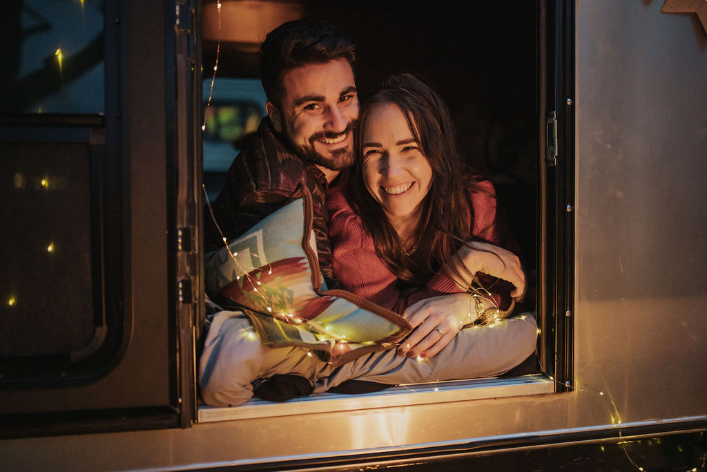 couple snuggle in their vintage trailer with twinkle lights after getting engaged