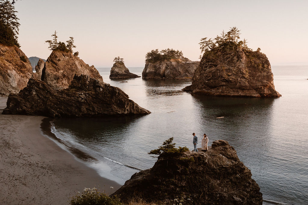 couple stands on a cliff at sunset for their elopement at Secret Beach in Brookings, Oregon