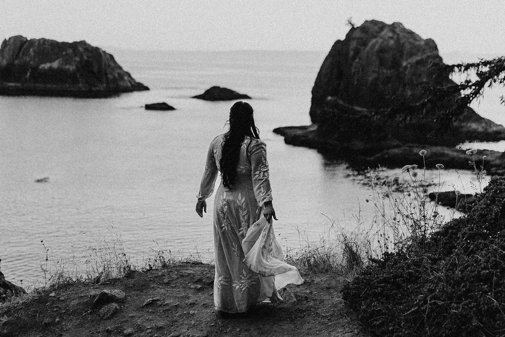 black and white image of a bride looking out over the ocean on her elopement day